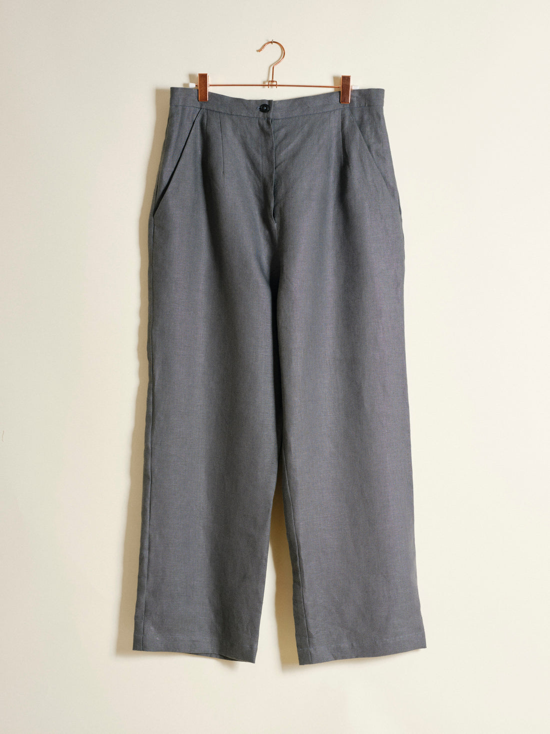 Gray pants hanging on a wooden hanger against a beige background
