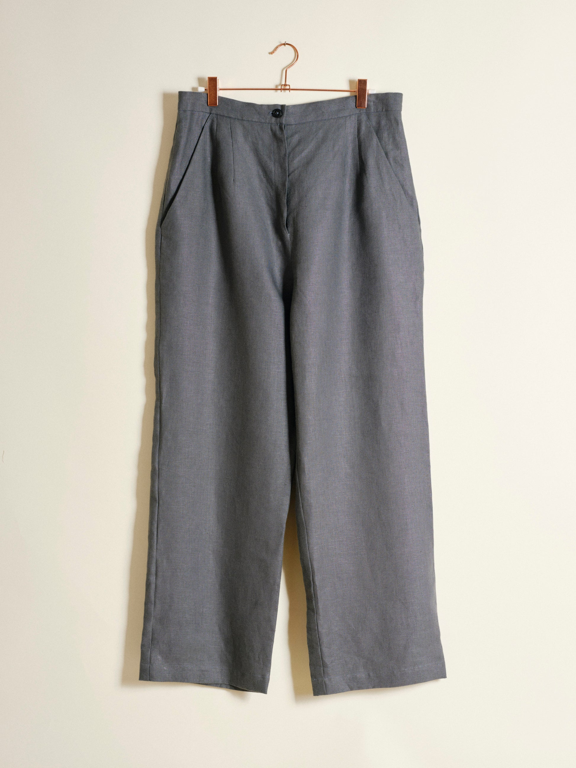 Gray pants hanging on a wooden hanger against a beige background