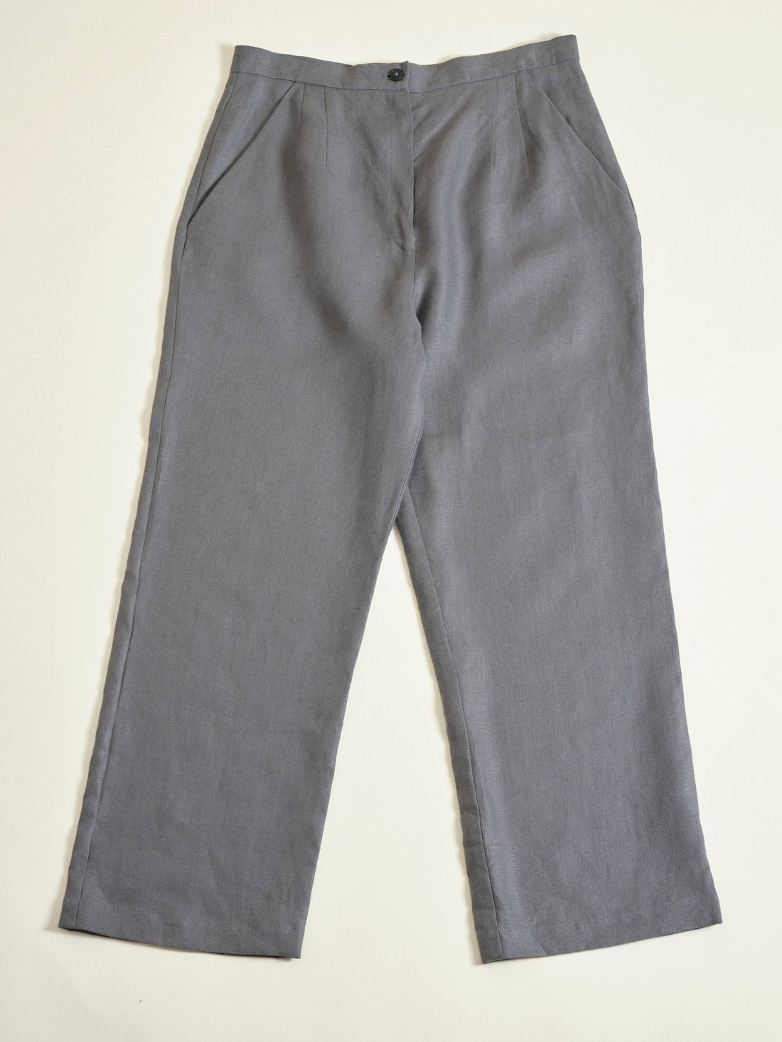 Gray pants hanging on a wooden hanger against a beige background