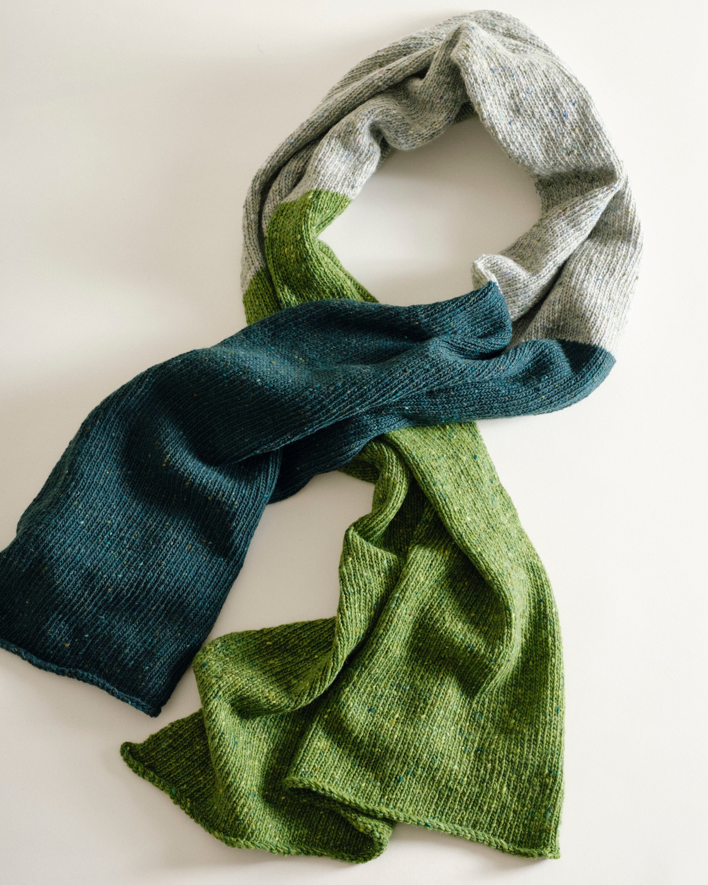 Three knitted scarves in gray, blue, and green on a light background